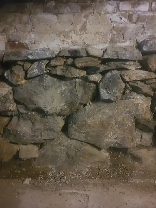 typical foundation construction. brick on top, stone on bottom. Notice there is a little dampness in the dirt coming through.