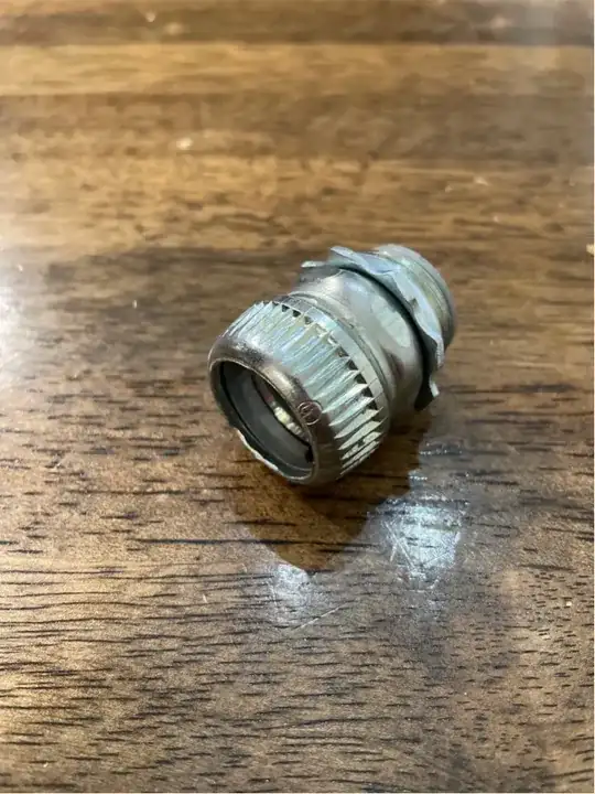 A picture of the mystery item (an EMT box connector) sitting on a wooden tabletop.