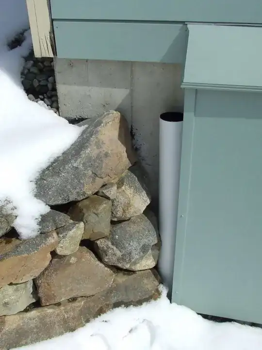 Polyethylene sewer pipe emerging from ground exterior, adjacent to foundation