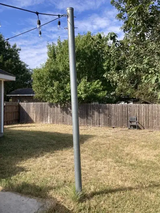 4 inch pole with party lights attached, leaning slightly toward concrete patio