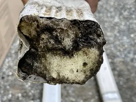Downspout clogged by brown/black and beige foam-like substance