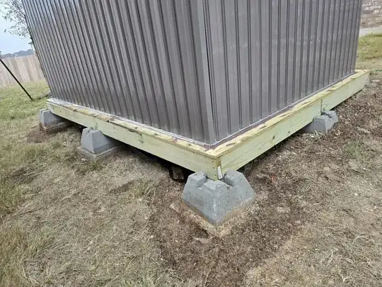 pressure-treated base of shed resting on concrete footers above the soil
