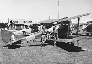 Two airmen assigned to No. 7 Elementary Flying School with two of the unit's Tiger Moth aircraft at Western Junction Aerodrome