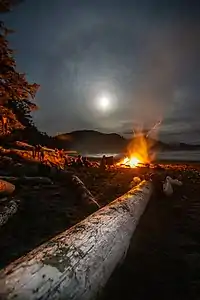 Halo moon above a campfire on a sand beach on the ocean with mountains in the background