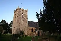 Church with substantial tower under a sky of duck-egg blue, with a large Yew on the right., a very dark green. The tower is broad, but barely higher than the deeply pitched roof on the nave. It has a clockface on the nearest side.