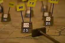 A wooden marker on a map, surrounded by several others. Below and to the right is a cue with a wooden slab on the end, used to move the markers.
