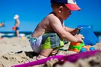 Image 6An infant boy playing with a toy dump truck at the beach. (from Boys' toys and games)