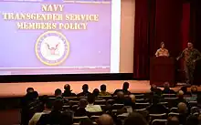 Training is being conducted to educate Naval War College personnel ofr United States Navy transgender policies on January 10, 2017. View is from the audience showing a majority of the screen, with the lecturers (Captain Tamara Graham and Command Master Chief Craig Cole) standing to the right of the screen at a lectern, facing the audience.