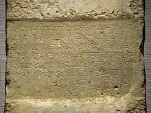 Large square marble slab that has been engraved. The inscription states: "Beside these walls of Serapis the warden of the temple Karneades of Barke, son of Eukritos, o foreigner, and his spouse Pythias and his daughter Eraso placed to Hestia a pure altar, as a reward for this, o you that governs the marvelous dwellings of Zeus, grant to them a lovely auspiciousness of life."