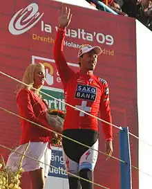 A man walking across a stage while waving and wearing a red jersey