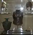Hoplite armour exhibit. Note the gold inserts around the chest area of the bronze upper torso plate at the centre of the exhibit. The helmet on the upper left is a restored version of the oxidised helmet on the right.