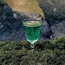 An ornate glass with green fluid in it, sitting in grass
