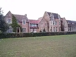 Range of dressed stone Tudor styled buildings stretching left to right, with grass playing fields to front