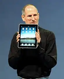 A bespectacled, bearded Steve Jobs holding a tablet