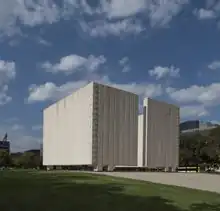 Designed by architect Philip Johnson and erected in 1970, the concrete memorial to President Kennedy dominates a square in downtown Dallas near Dealey Plaza, where the president was assassinated. Johnson's design is a cenotaph, or open tomb, that symbolizes the freedom of Kennedy's spirit. The memorial is a square, roofless room, 30 feet high and 50 x 50 feet wide with two narrow openings facing north and south.