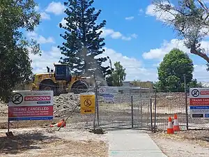 A pedestrian crossing across the railway which has been blocked off. Behind is rubble and a construction vehicle.