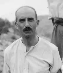 Black-and-white photograph of a moustachioed man, facing the camera, with an open-necked shirt.