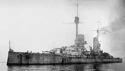 A large, light gray warship sits motionless in a calm sea