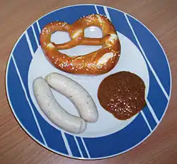 Plate with pretzel, sausage, and brown mustard
